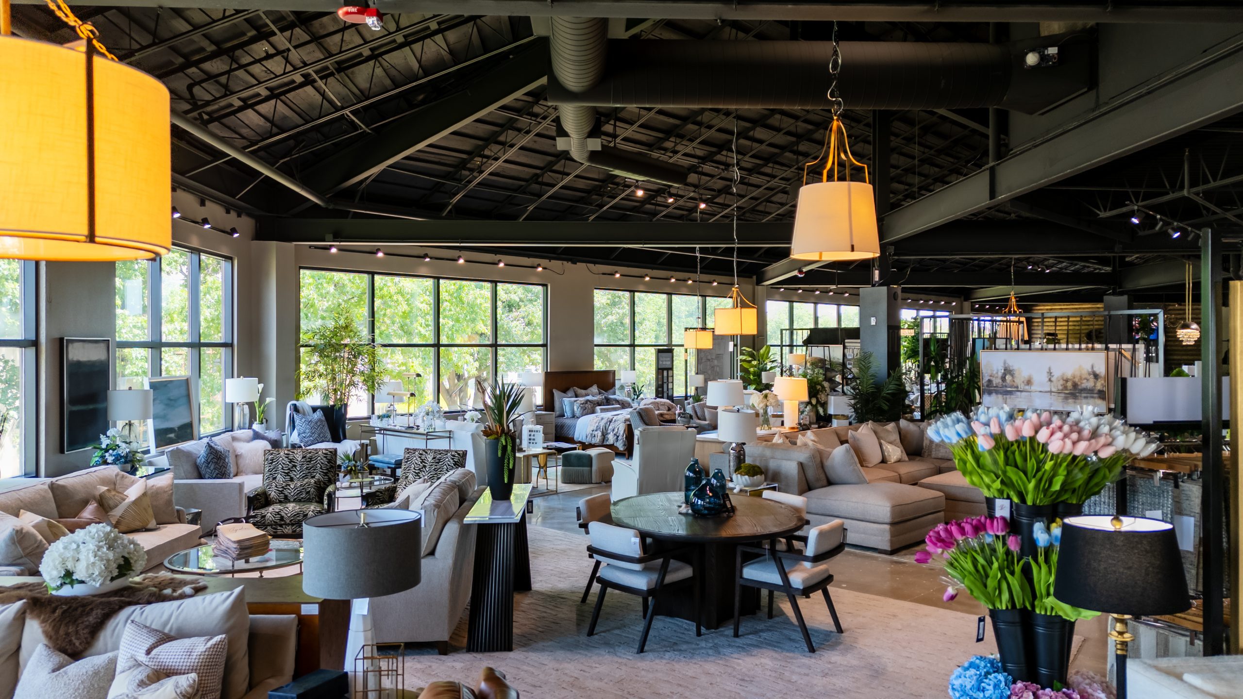 Inside the Louis Alan Design Gallery showroom on East 61st in Tulsa — sofas, dining vignettes, lighting, and floral arrangements beneath tall windows